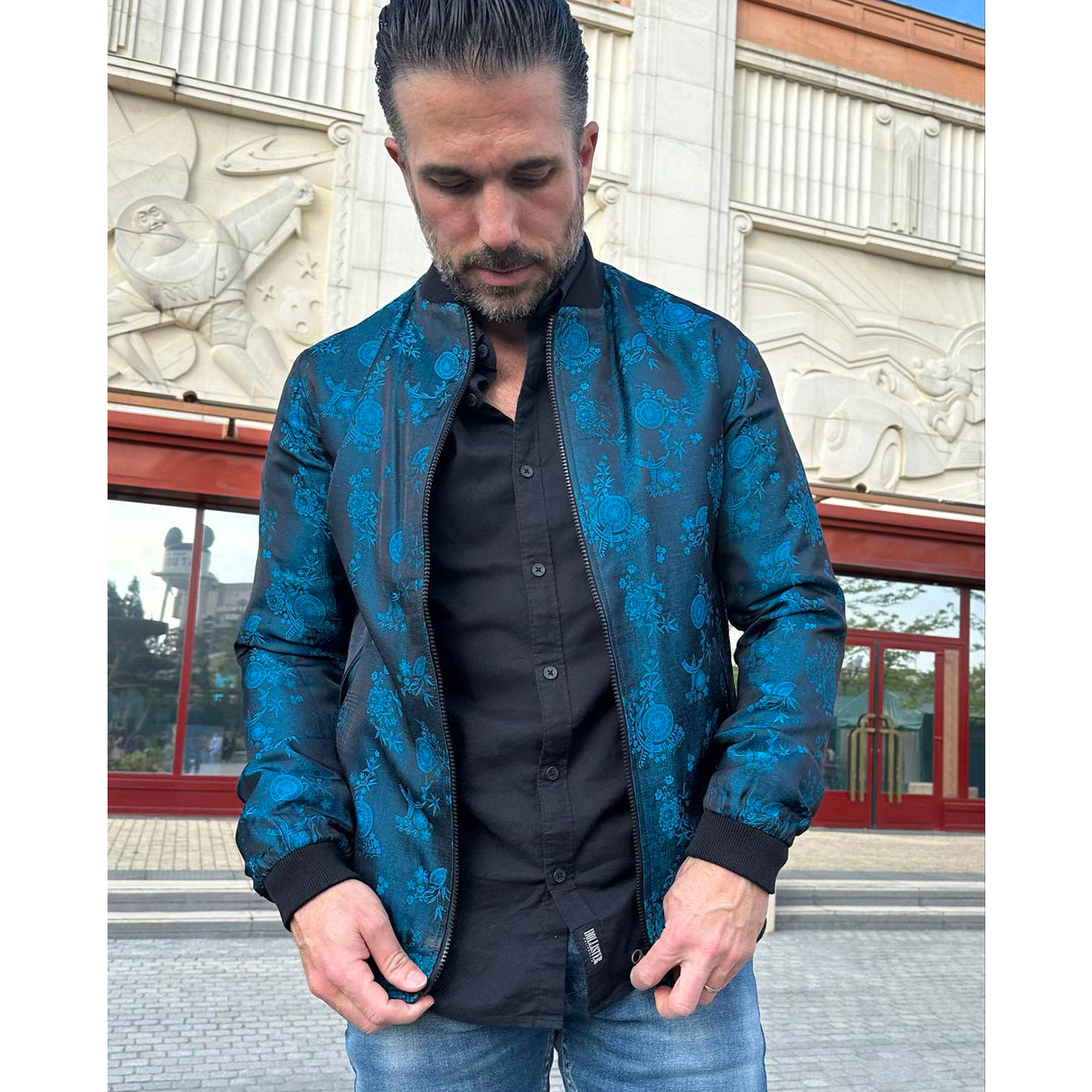 Geoffroy wearing a Kaelu silk bomber jacket in a casual chic outfit with jeans and black shirt