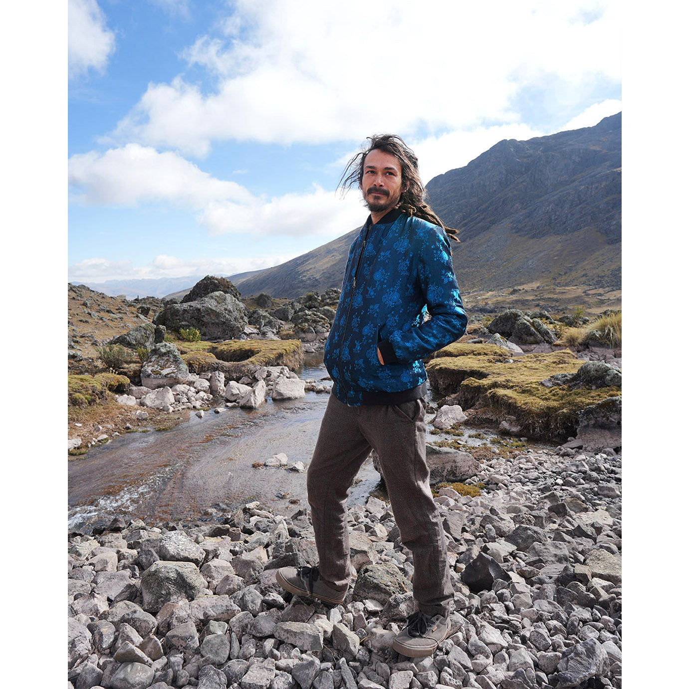 Joshua hiking near Ausangate mountain wearing a Kaelu silk bomber jacket, showcasing its stylish and durable design.