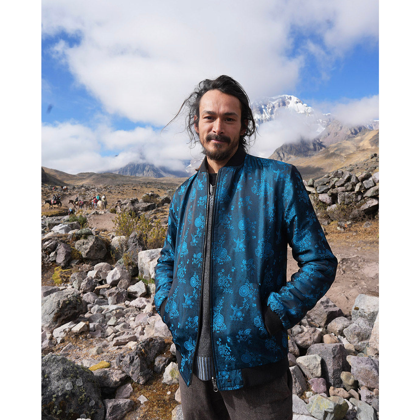 Joshua wearing his Kaelu blue silk bomber jacket in the Andes, highlighting its quality craftsmanship and adventure-ready look.