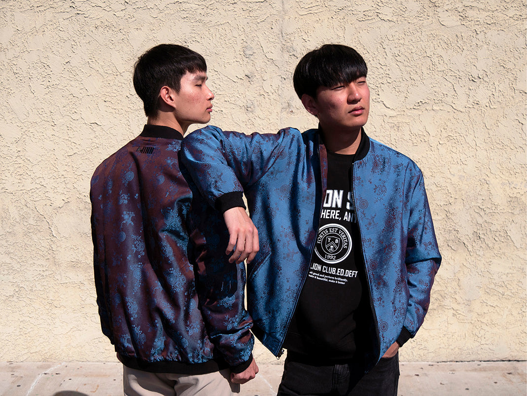 Xeon and Ryong wearing different sides of the Kaelu silk bomber jacket in Korea Town Los Angeles — one in a light grey urban look, the other in a relaxed dark grey outfit.