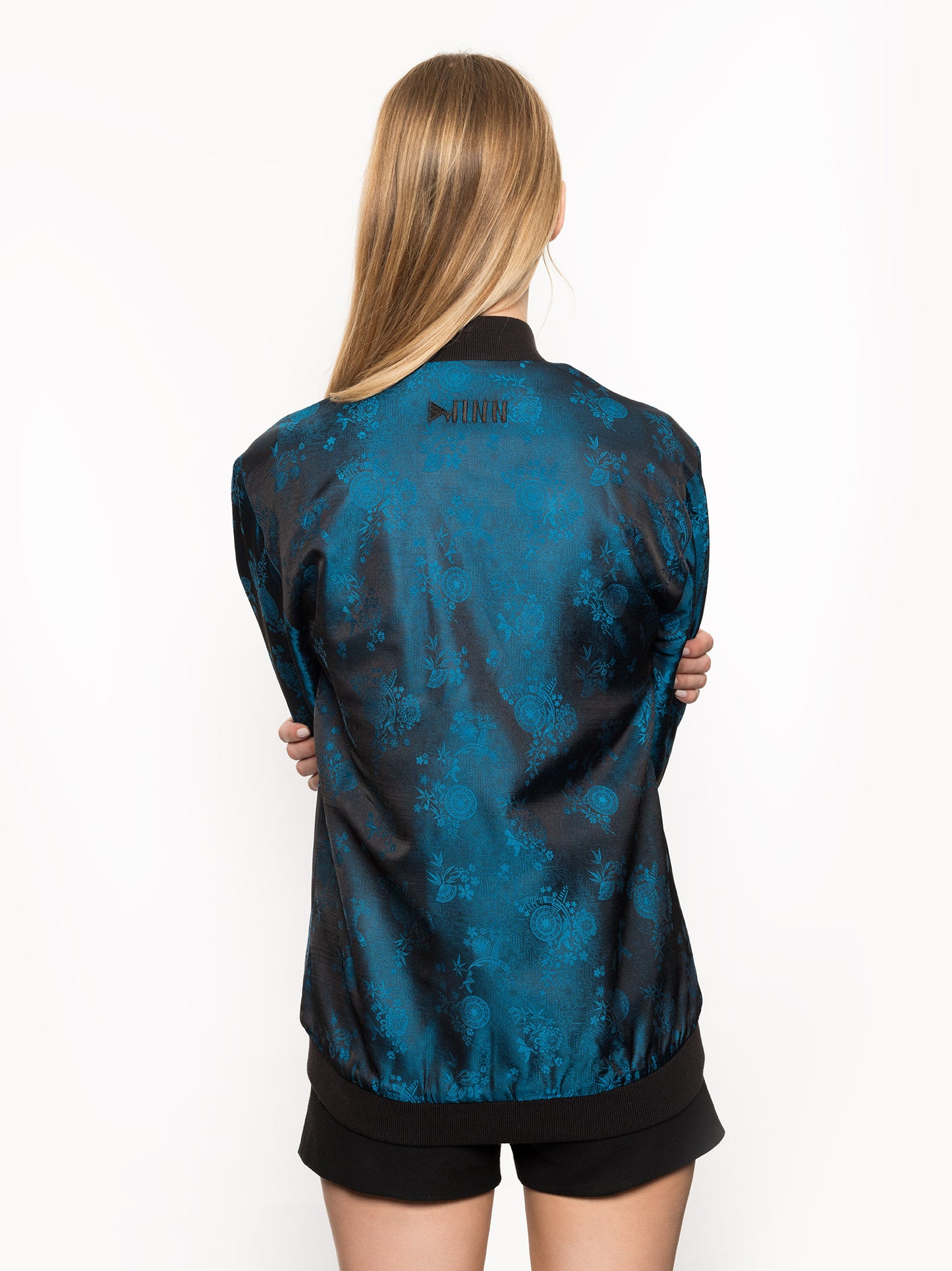 Kaelu's limited edition 'DJINN' silk bomber jacket, numbered 1 to 20. Handcrafted in Vietnam with authentic Vietnamese silk, this reversible jacket offers versatility with one side in striking blue and the other in sleek black. Combining Asian luxury with urban style, it's fairtrade and fashion-forward, epitomizing streetwear sophistication. Back shot.