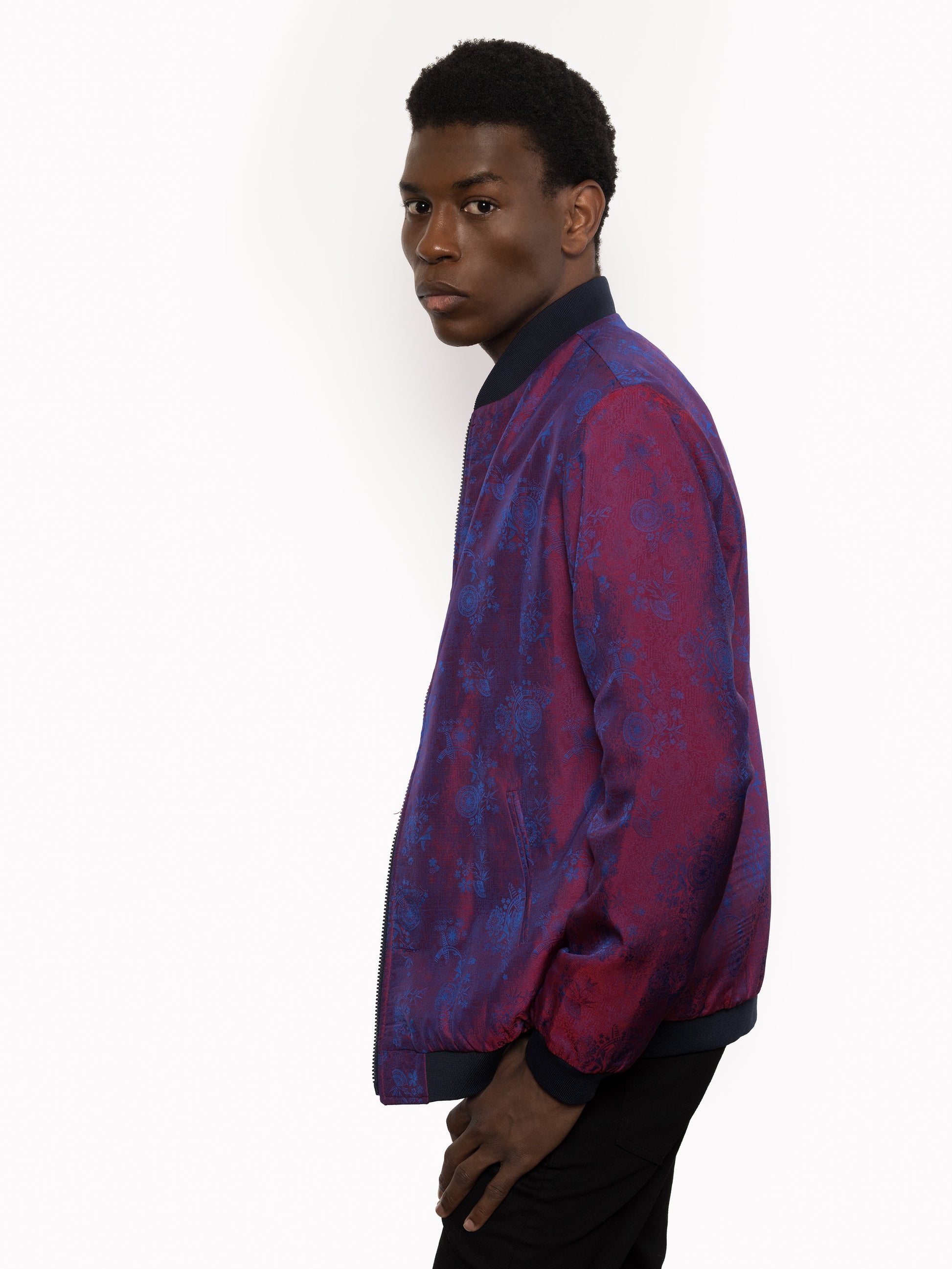 "Presenting Kaelu's exclusive 'DJINN' silk bomber jacket, numbered 1 to 20. Handcrafted in Vietnam from authentic Vietnamese silk, this reversible masterpiece offers two distinct hues of purple: one leaning towards a deep blue-purple, the other towards a soft pink-purple, complementing black skin tones impeccably. Embrace understated elegance with this piece, a departure from the vibrant Japanese sukajan, exuding sophistication in every detail."