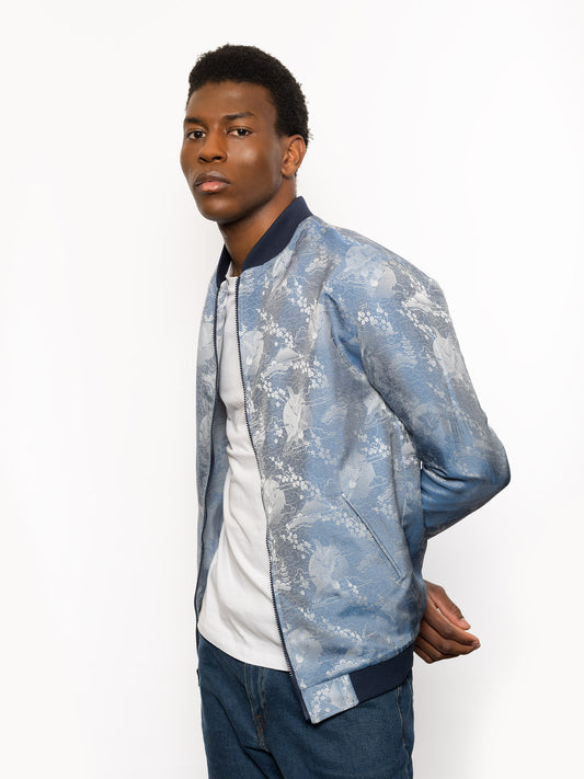 "Introducing Kaelu's exclusive 'DJINN' silk bomber jacket, numbered 1 to 20. Handcrafted in Vietnam with authentic Vietnamese silk, this reversible wonder showcases a stunning combination of silver and blue, adorned with graceful heron bird and mount fuji motifs. A true standout piece, offering a departure from the traditional, it's a symbol of sophistication and urban flair."