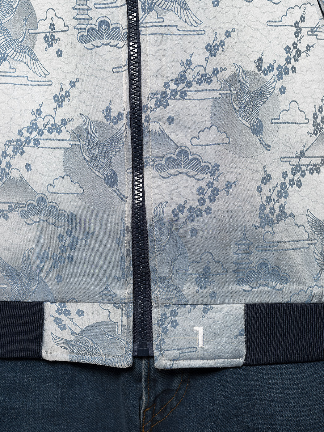 "Introducing Kaelu's exclusive 'DJINN' silk bomber jacket, numbered 1 to 20. Handcrafted in Vietnam with authentic Vietnamese silk, this reversible wonder showcases a stunning combination of silver and blue, adorned with graceful heron bird and mount fuji motifs. A true standout piece, offering a departure from the traditional, it's a symbol of sophistication and urban flair."