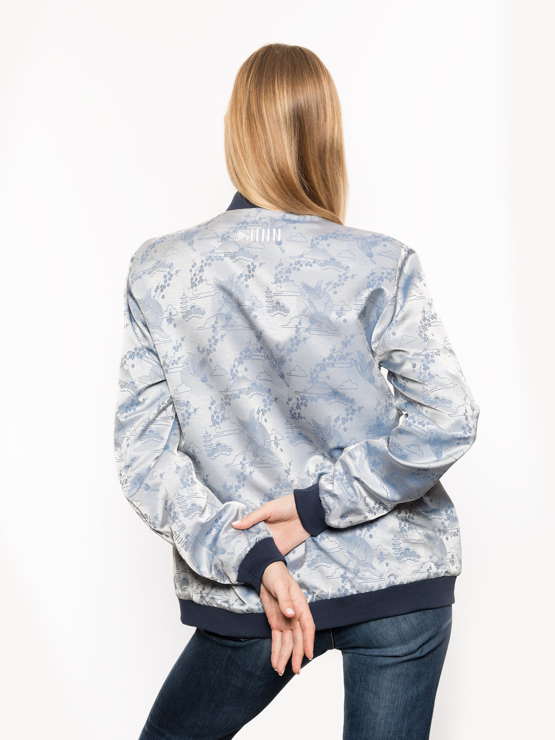 "Introducing Kaelu's exclusive 'DJINN' silk bomber jacket, numbered 1 to 20. Handcrafted in Vietnam with authentic Vietnamese silk, this reversible wonder showcases a stunning combination of silver and blue, adorned with graceful heron bird and mount fuji motifs. A true standout piece, offering a departure from the traditional, it's a symbol of sophistication and urban flair."