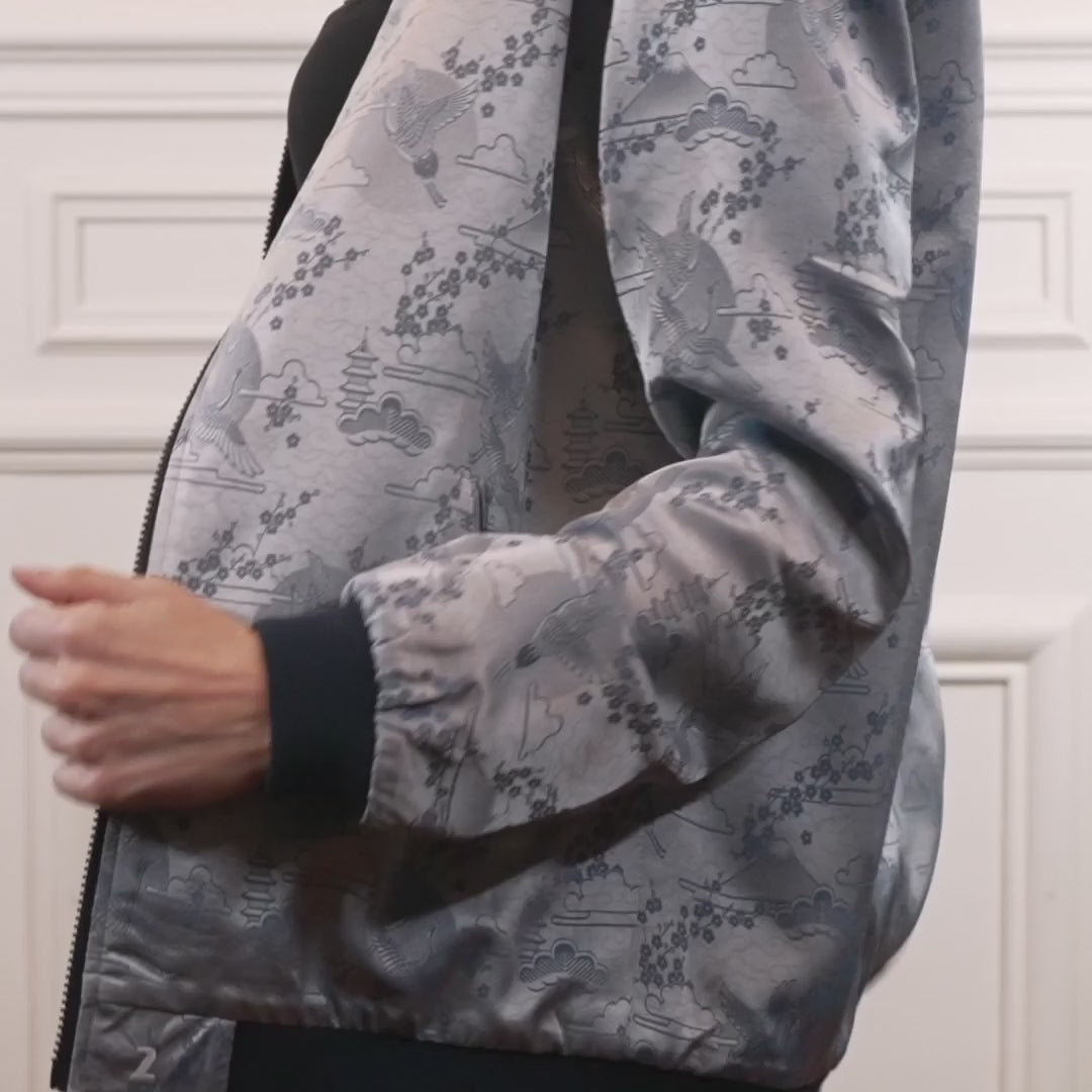 "Introducing Kaelu's exclusive 'DJINN' silk bomber jacket, numbered 1 to 20. Handcrafted in Vietnam with authentic Vietnamese silk, this reversible wonder showcases a stunning combination of silver and blue, adorned with graceful heron bird and mount fuji motifs. A true standout piece, offering a departure from the traditional, it's a symbol of sophistication and urban flair."