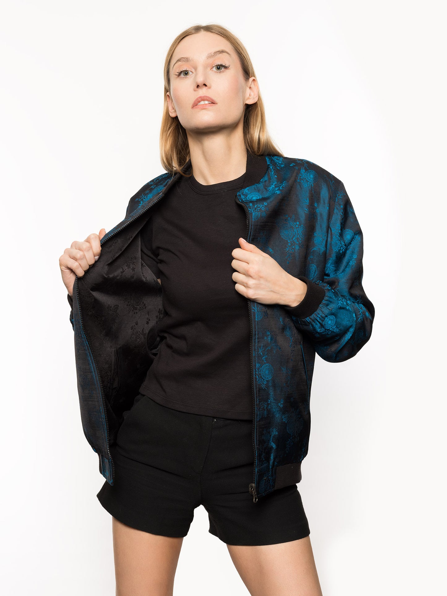 Kaelu's limited edition 'DJINN' silk bomber jacket, numbered 1 to 20. Handcrafted in Vietnam with authentic Vietnamese silk, this reversible jacket offers versatility with one side in striking blue and the other in sleek black. Combining Asian luxury with urban style, it's fairtrade and fashion-forward, epitomizing streetwear sophistication. Front shot for her.