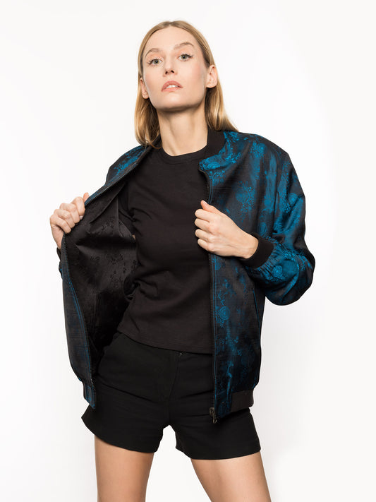 Kaelu's limited edition 'DJINN' silk bomber jacket, numbered 1 to 20. Handcrafted in Vietnam with authentic Vietnamese silk, this reversible jacket offers versatility with one side in striking blue and the other in sleek black. Combining Asian luxury with urban style, it's fairtrade and fashion-forward, epitomizing streetwear sophistication. Front shot for her.